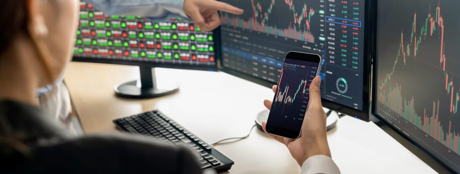 A cropped image of smart businessman analysis growth stock graph displayed in mobile phone while discussion about financial investment at stock market with computer displayed graph. Burgeoning.