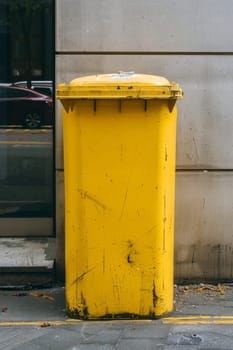 A yellow recycling container is on the street.