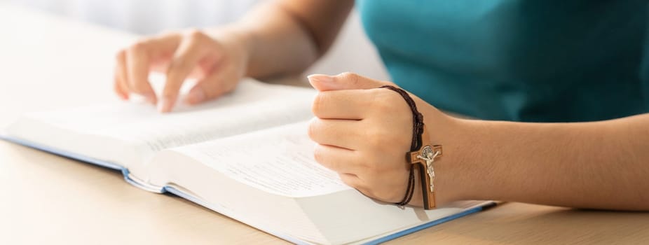 Cropped image of female reading a bible book while holding cross at wooden table with blurring background. Concept of hope, religion, faith, christianity and god blessing. Warm. Burgeoning.