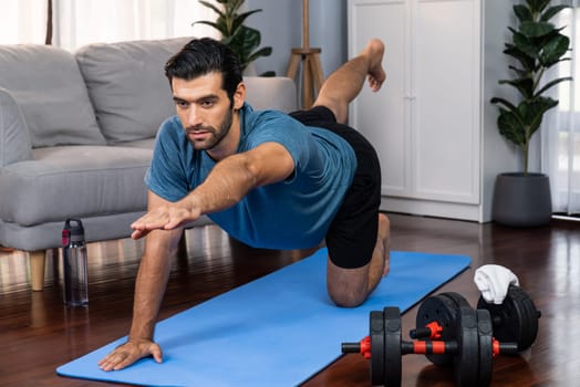 Flexible and dexterity man in sportswear doing yoga position in meditation posture on exercising mat at home. Healthy gaiety home yoga lifestyle with peaceful mind and serenity.