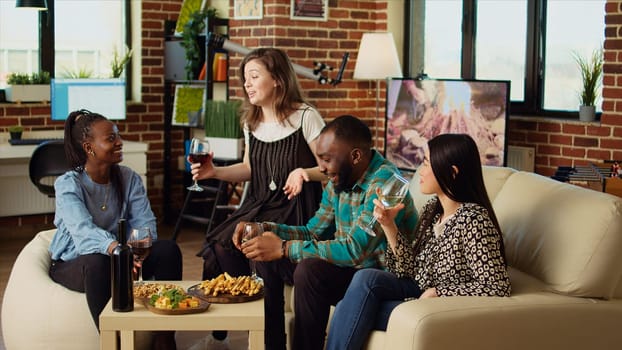 Woman telling interesting story to happy apartment party guests during weekend gathering, gossiping about friend. Friends listening to funny tale from host while drinking wine and eating snacks