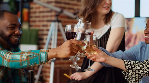 Close up shot of wine glasses being toasted at home party by multiethnic group of people celebrating their friendship together. Friends having reunion gathering, enjoying charcuterie board snacks