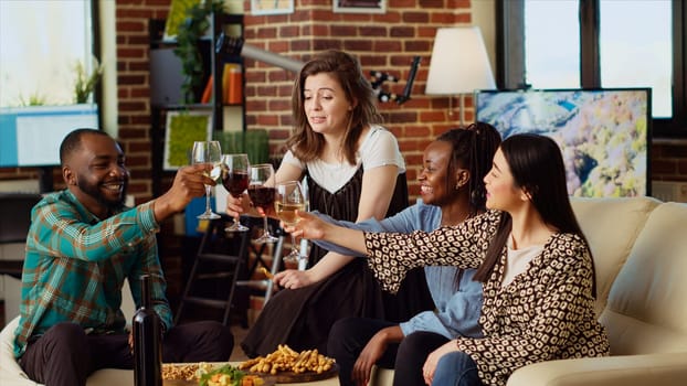 Multiracial group of people celebrating their friendship together, toasting wine and champagne glasses at home party. Joyful friends having reunion gathering, enjoying alcoholic drinks