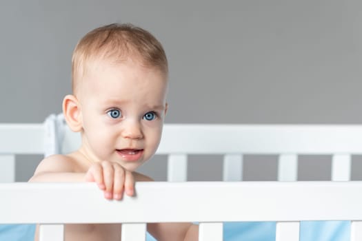 Baby with a vaguely distorted facial expression in a white classic crib.