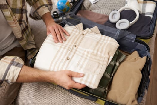 Male hands, tourist packing his clothes in luggage, putting items inside suitcase, getting ready for a vacation, going on holiday or business trip.