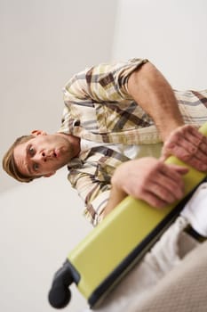 Vertical shot of man trying to press suitcase and close zipper, packing clothes for vacation. Tourist going on holiday, preparing for travelling abroad. Tourism concept