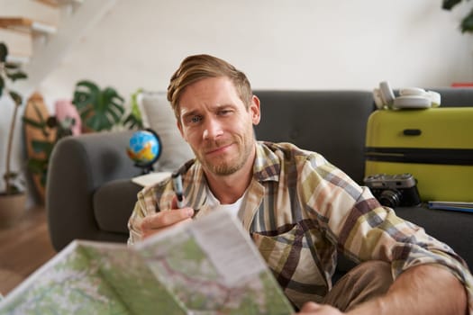 Smiling handsome man, traveller going on holiday, holding road map, planning his holiday, choosing the route.