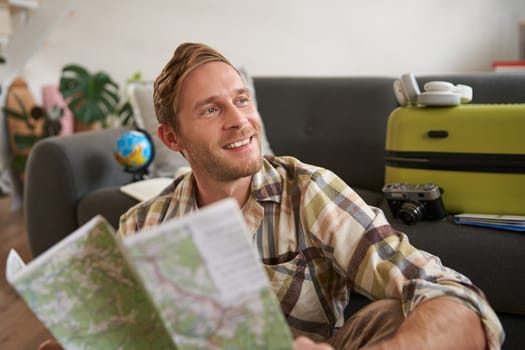 Portrait of handsome smiling guy, tourist going on holiday, holding map, plans where to go on vacation.