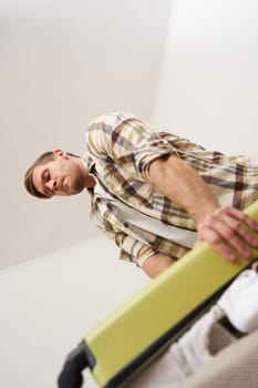 Vertical shot of man trying to press suitcase and close zipper, packing clothes for vacation. Tourist going on holiday, preparing for travelling abroad. Tourism concept