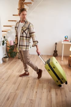 Vertical shot of young man carrying a suitcase, going on vacation, walking with luggage. Travelling and people concept
