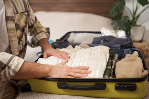 Cropped shot of male hands, tourist puts his clothes in suitcase, packs luggage for holiday trip, goes on vacation.