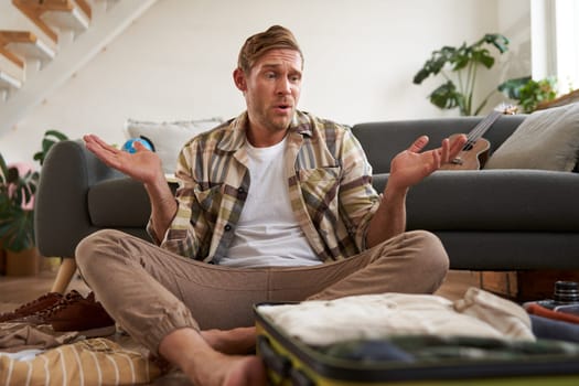 Man packing suitcase, shrugging, deciding what to bring on holiday, looking confused.