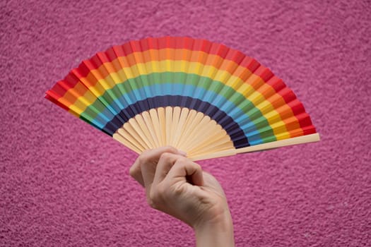 A hand holding a rainbow fan isolated on violet background. Concept of LGBTQ community support.