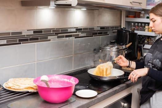 A young home cook carries a fried pancake onto a plate. Tasty homemade pancakes from a young woman's hand.