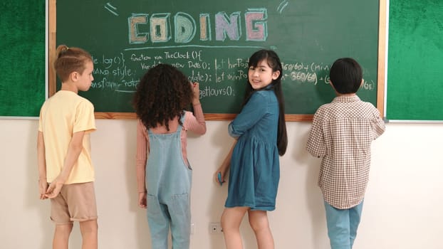 Back view of multicultural student writing prompt at board while skilled girl looking at camera while crossing arm with confident. Group of happy children planning idea by using blackboard. Pedagogy.