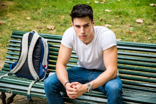 A man sitting on a bench with a back pack. Photo of a man sitting on a bench with a backpack