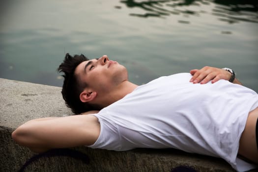 A man laying on a wall next to a body of water. Photo of a man relaxing by the water's edge