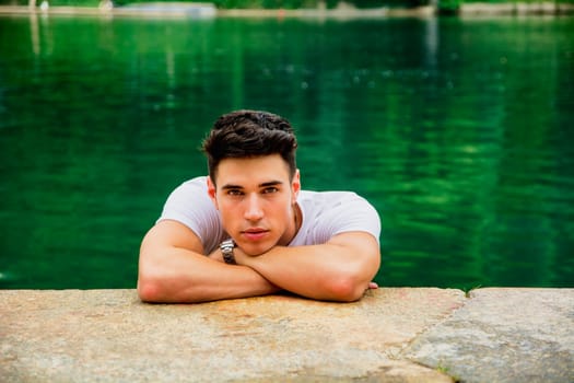 A man leaning his head on a rock next to a body of water. Photo of a man resting his head on a rock by the water's edge