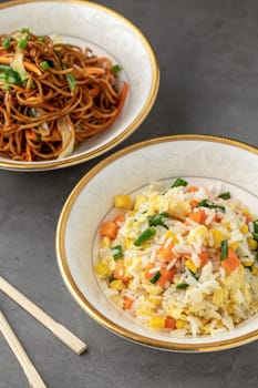 Noodles with vegetables and rice pilaf with egg and corn in a white bowl on a dark background