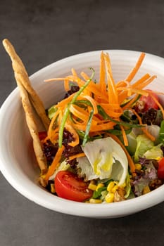 Salad with carrots, tomatoes, corn and lots of greens on a white porcelain plate