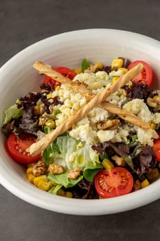 Mediterranean salad with goat cheese in white porcelain bowl on stone table