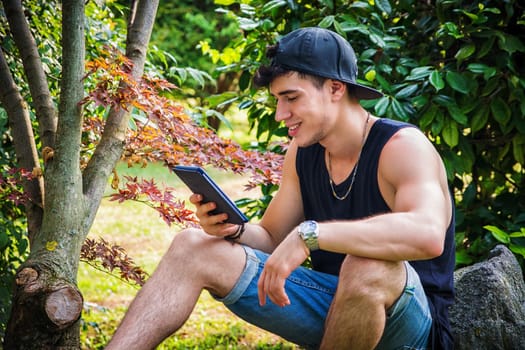 A man sitting on a rock looking at a tablet. Photo of a man sitting on a rock engrossed in his ebook reader