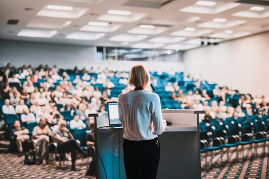 Female speaker giving a talk on corporate business conference. Unrecognizable people in audience at conference hall. Business and Entrepreneurship event