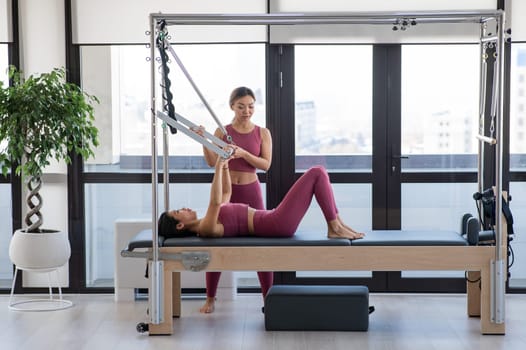 Asian woman doing pilates with trainer on cadillac reformer