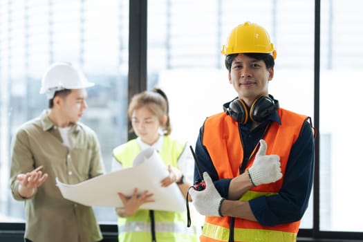 Portrait of civil engineer with hard hat holding radio walkie talkie while supervisor engineers and architect planning in background.