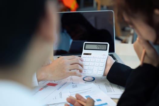 Businesswoman using a calculator to calculate numbers on a company's financial documents, analyzing historical financial data to plan how to grow the company. Financial concept..