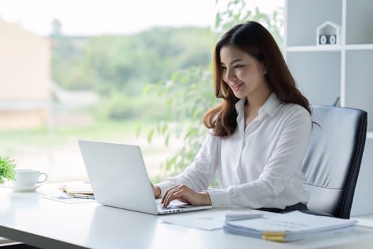 Asian Businesswoman sitting at her desk and busy working on a laptop in office.