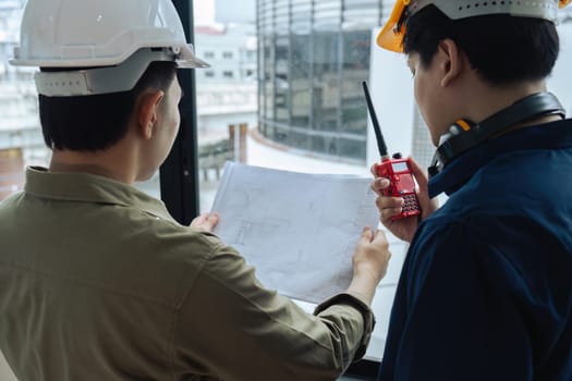 Civil engineers and architects inspecting and working building site with blueprints and holding walkie talkie.