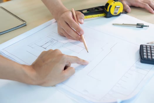 Close up of civil male engineer asian working on blueprint architectural project at construction site at desk in office.