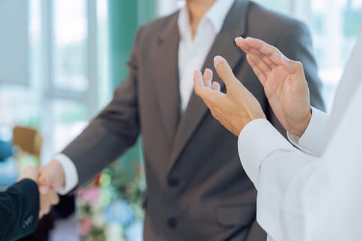 colleagues clapping hands while professional successful businesspeople in formal suit standing shaking hands greeting celebrating in company office.