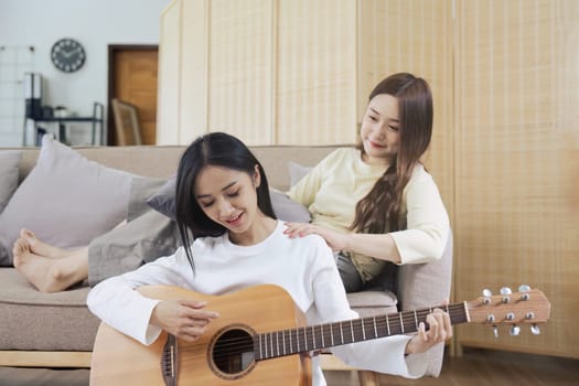LGBTQIA lesbian gay couple playing guitar and singing with romantic feelings at home.