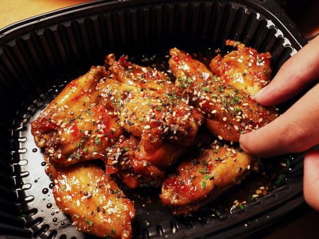 Man's hand picking up a Korean Chicken wings with sauce. 치킨. Asian street food. Delivery concept