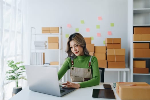 Starting small business entrepreneur of independent young Asian woman online seller is using computer and taking orders to pack products for delivery to customers. SME delivery concept.