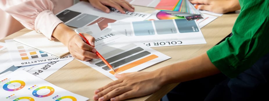 Cropped image of professional interior designers discuss and brainstorm main theme color in project on meeting table with color palette scatter around. Creative interior design concept. Variegated.