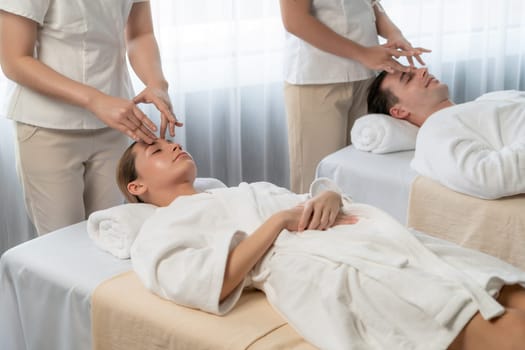 Caucasian couple enjoying relaxing anti-stress head massage and pampering facial beauty skin recreation leisure in dayspa modern light ambient at luxury resort or hotel spa salon. Quiescent