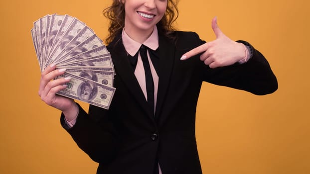 Woman pointing towards a stack of money with her finger isolated on yellow background.