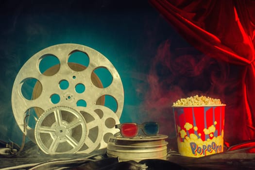 Old film reels, popcorn and 3d glasses on the table. Focus on glasses. Multicolored background. Evolution Film Media