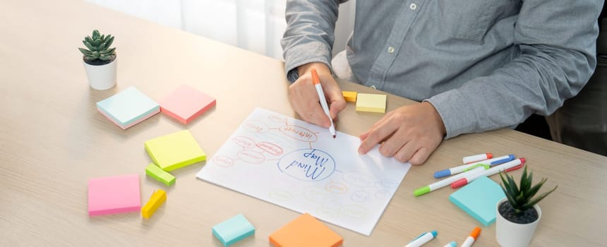 Skilled businessman brainstorms marketing ideas using mind maps. Successful male startup leader drafts financial plan on table with sticky notes scatter around. Closeup. Focus on hand.Variegated.