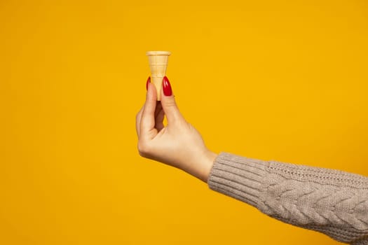 Woman hand holding small blank crispy ice cream cone isolated on yellow background