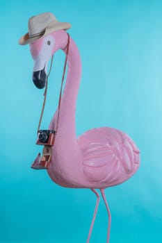 Figure of a pink flamingo tourist in a straw hat holding a camera