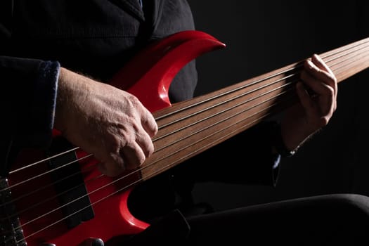 Male musician playing six-string fretless bass guitar on dark background