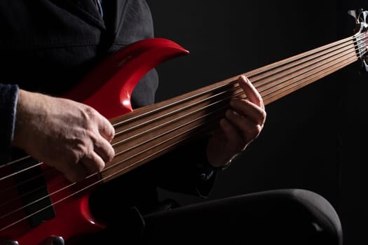 Male musician playing six-string fretless bass guitar on dark background