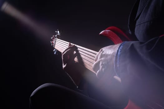 Male musician playing six-string fretless bass guitar on dark background