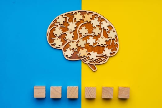 Mock up of a human brain with scattered puzzle pieces on a yellow and blue background. Six cubes in which you can write the word autism in your font.