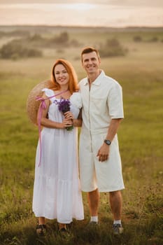 A couple in love in white clothes in a field at a red sunset.