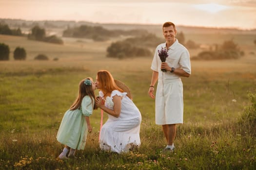 A beautiful happy family of three is standing in a field at sunset.
